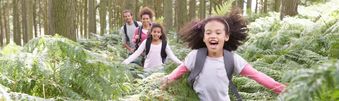 girl running in the woods with parents and sibling behind her
